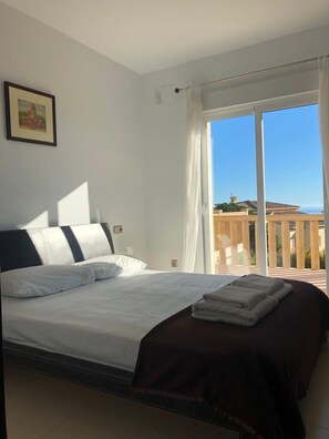 A bedroom with a bed, a picture on the wall, and a balcony with a view.