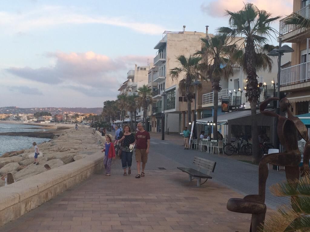 Une promenade en bord de mer, avec un chemin pavé, des palmiers et des bâtiments dotés de balcons.
