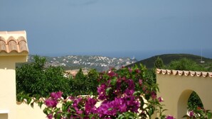 A view of a coastal town with buildings on a hillside, a clear sky, and purple flowers in the foreground. - Villa Zoe - 4 bed - sleeps 8 - sea views - BOOK NOW!!!! (Benitachell, Alicante)