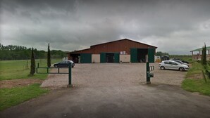 Ein großes Industriegebäude mit Schotterweg und grünem Tor.