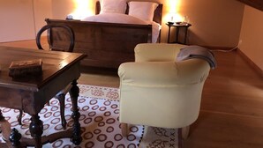 Ein Schlafzimmer mit einem hölzernen Bett, einem kleinen Tisch, einem Sessel und einem Nachttisch mit Lampe.
