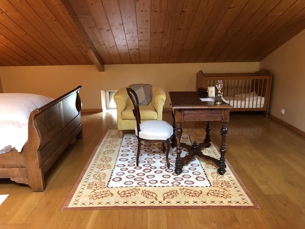 Un dormitorio acogedor en un ático con una cama de madera, un sillón amarillo, una mesa de madera con una vela y una alfombra estampada.