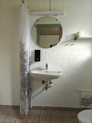 A bathroom with a white sink, a round mirror, a shower curtain, and a toilet. - Nordgården Pension (Samsø)
