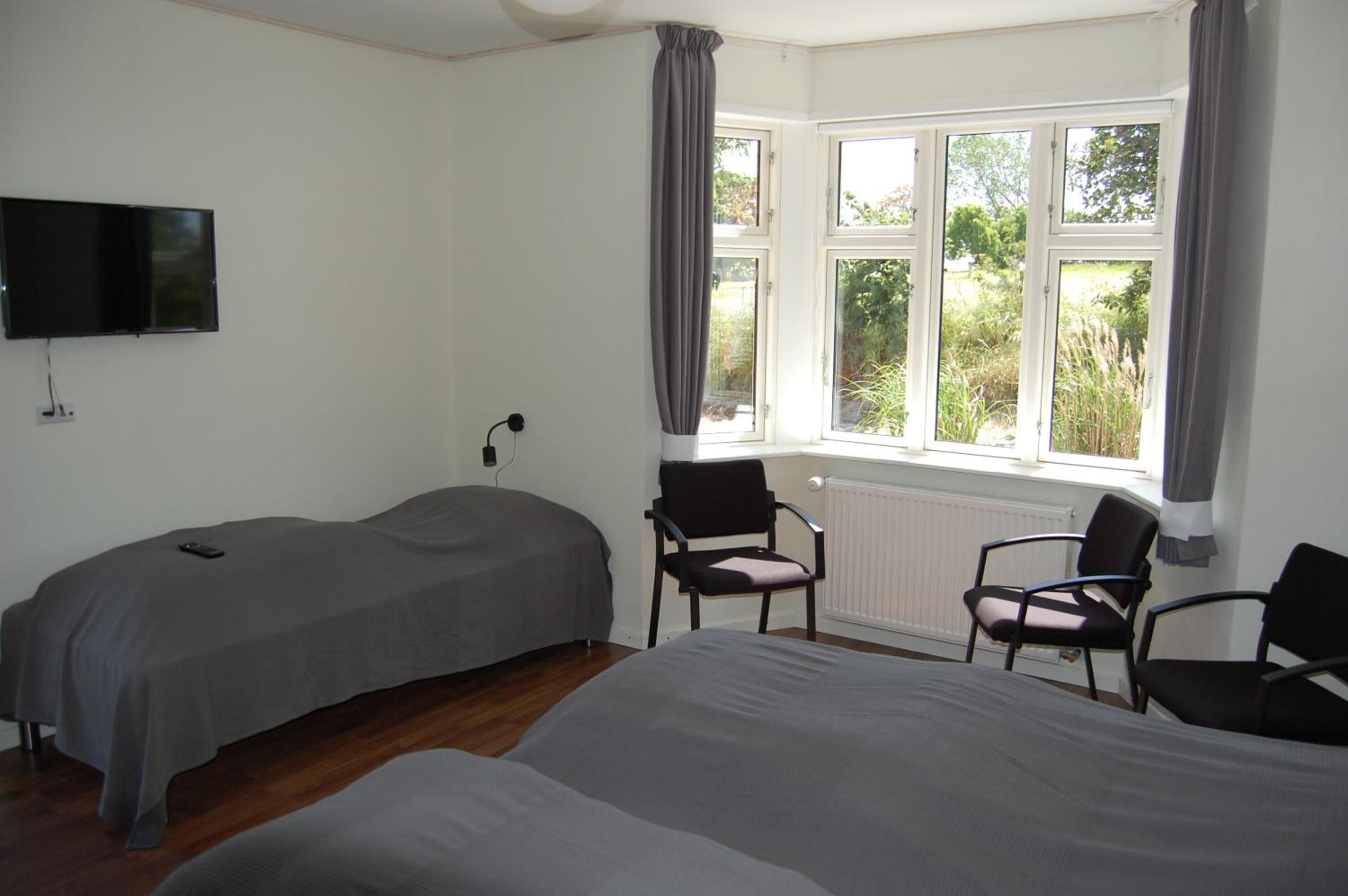 A bedroom with two beds, a TV, and a window with curtains.