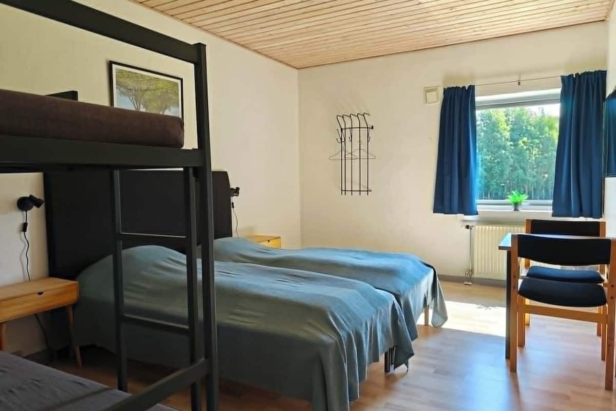 A room with bunk beds, a desk, a chair, a radiator, and a window with curtains.