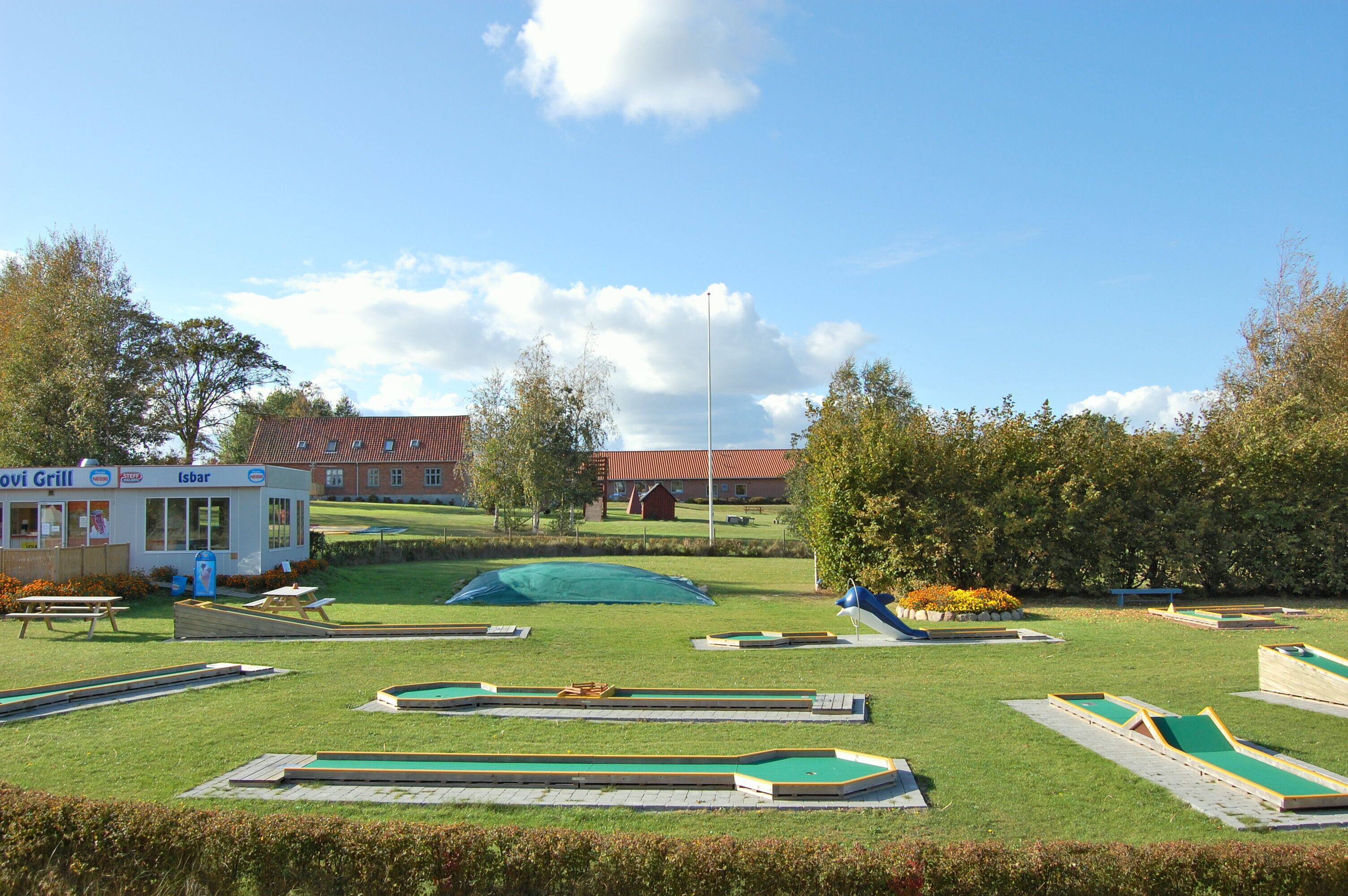 Un campo de prácticas de golf con múltiples calles verdes, un área de picnic y un pequeño edificio con la inscripción 'Isbar'.