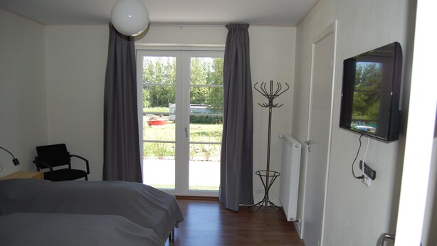 Un dormitorio con dos camas, una silla, un perchero y un televisor.