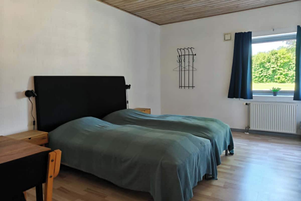 A room with a bed, a desk, a chair, a radiator, and a window with curtains.