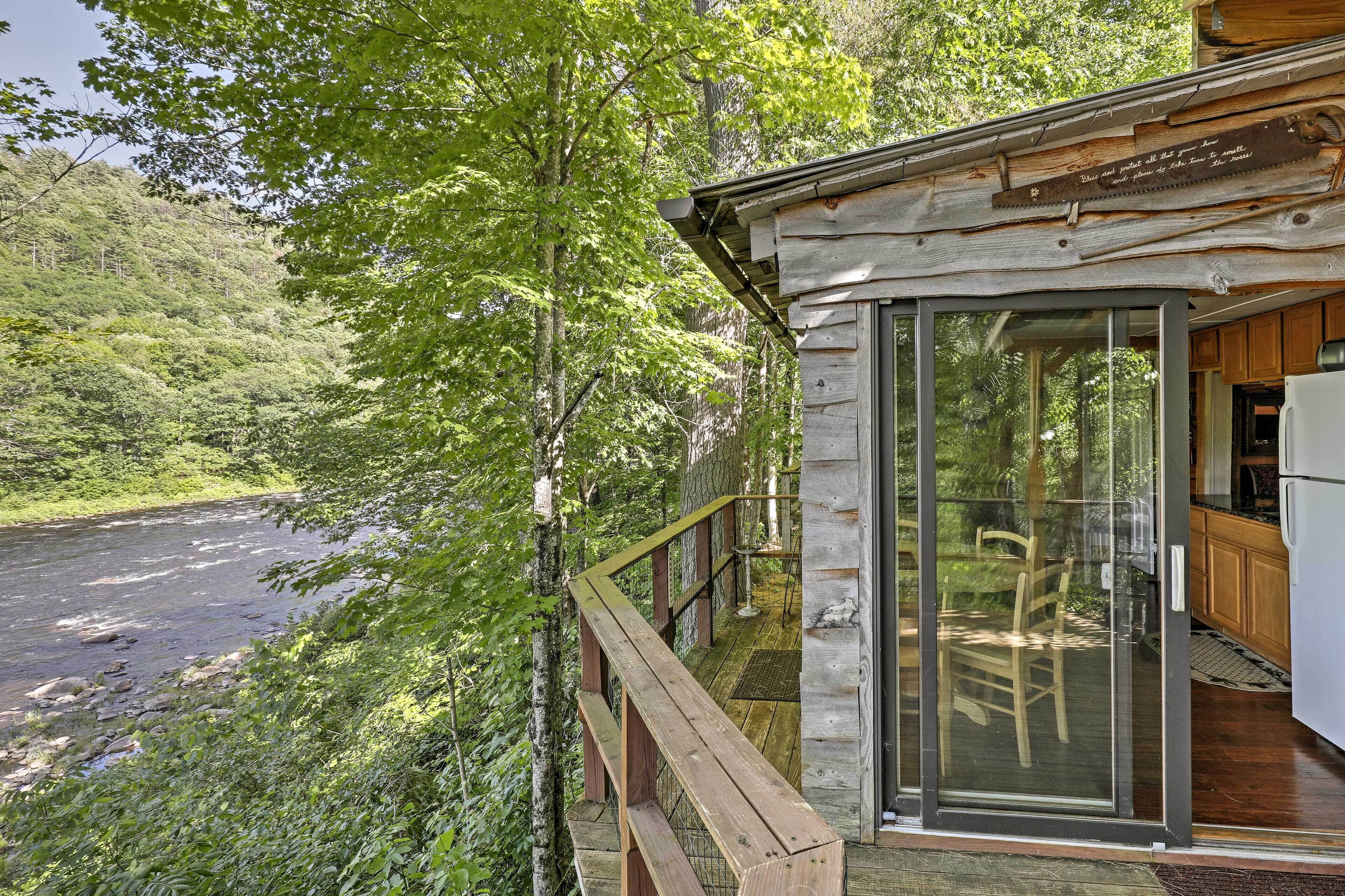 Una cabaña con puerta de cristal que da a una terraza, con vistas a un río rodeado de árboles.