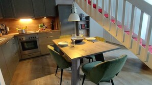 A modern kitchen with a dining area, featuring a wooden table, green chairs, and a staircase with red accents. - Tante Maaß – maisonette flat, shower, washing machine, parking space, TV, WiFi (Flensburg)