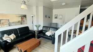 A living room with two black leather sofas, a wooden coffee table, and a large abstract painting on the wall. - Tante Maaß – maisonette flat, shower, washing machine, parking space, TV, WiFi (Flensburg)