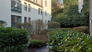 A pathway flanked by lush green hedges and a white building with multiple windows. - Tante Maaß – maisonette flat, shower, washing machine, parking space, TV, WiFi (Flensburg)