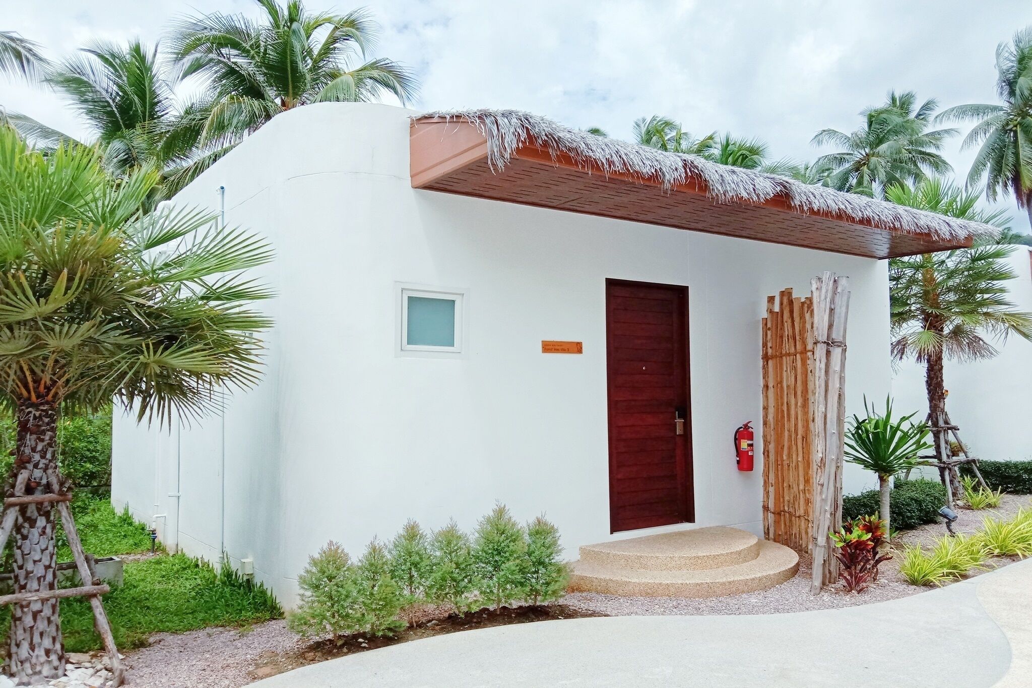 A small, single-story building with a white exterior, a wooden door, and a thatched roof.