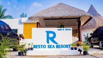Un resort con techo de paja, un letrero que dice 'Resto Sea Resort' y plantas en macetas al frente.