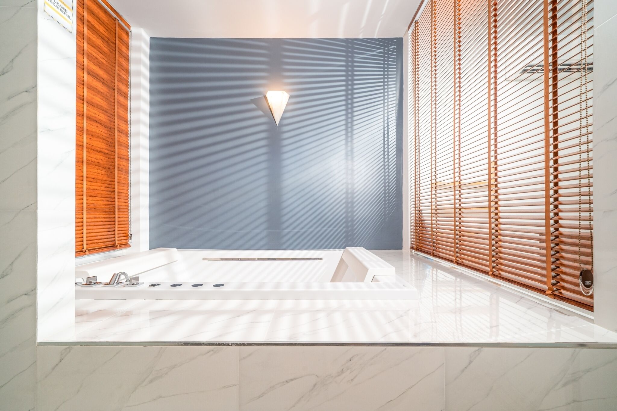A modern bathroom with a large bathtub, wooden blinds, and a marble countertop.