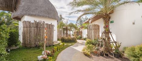 A pathway leading to thatched-roof cottages surrounded by lush greenery and potted plants.