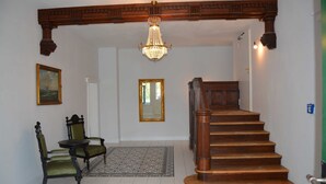 A staircase with wooden railings and a chandelier, a mirror, and two chairs with a rug on the floor. - Hirschaue - Redentin manor house (Krusenhagen)