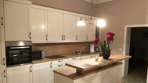 A modern kitchen with white cabinets, a built-in oven, a microwave, a sink, and a central island with a vase of red flowers. - Hirschaue - Redentin manor house (Krusenhagen)
