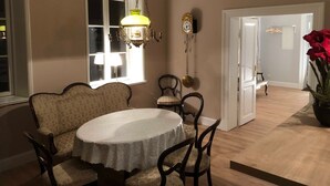 A dining area with a round table, chairs, a chandelier, a window, and a door leading to another room. - Hirschaue - Redentin manor house (Krusenhagen)