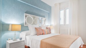 Quarto com cama, mesas de cabeceira e janela com cortinas.