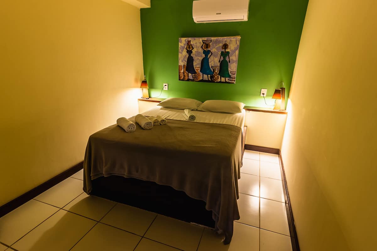A hotel room with a bed, a painting on the wall, and two bedside lamps.
