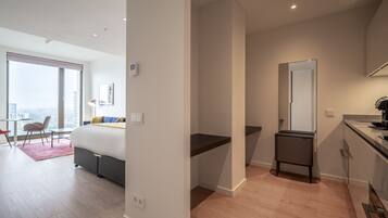 A modern hotel room with a large bed, a desk, a small bathroom, and a view of the city.