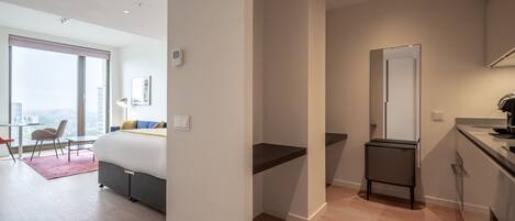 A modern hotel room with a large bed, a desk, a small bathroom, and a view of the city.
