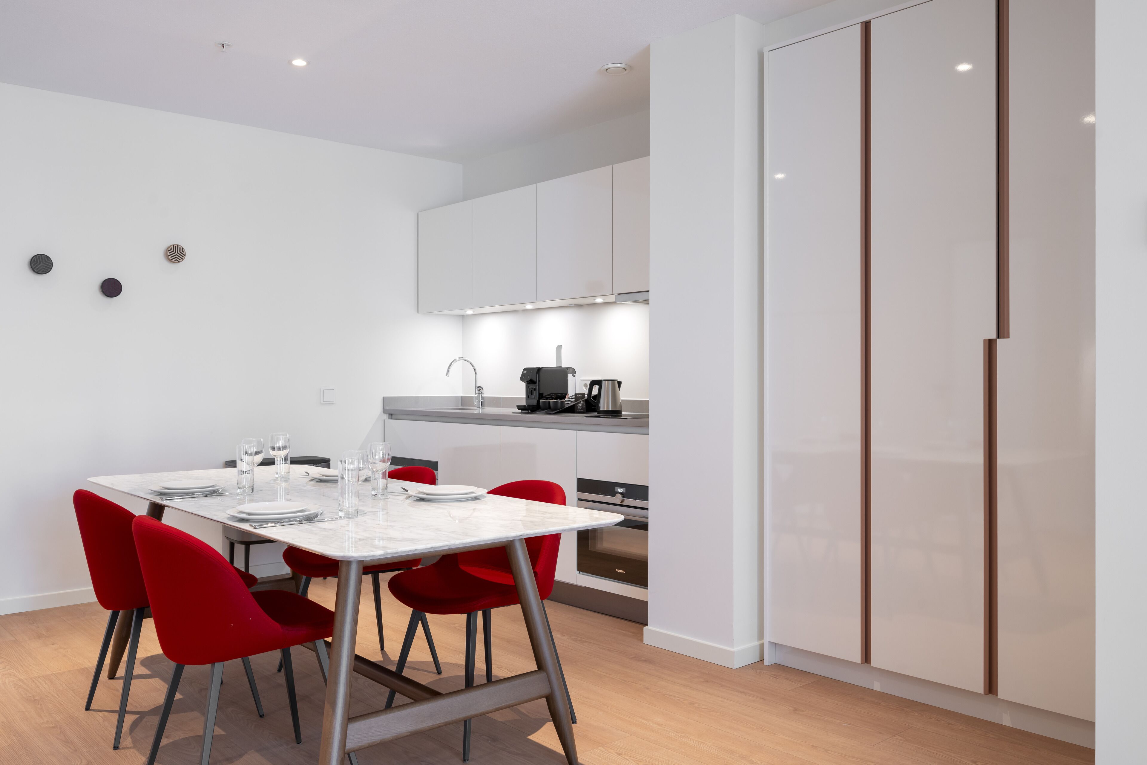 Een moderne keuken met witte kasten, een eettafel met rode stoelen en een inbouwoven.