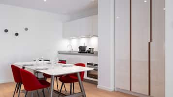 Een moderne keuken met witte kasten, een eettafel met rode stoelen en een inbouwoven.