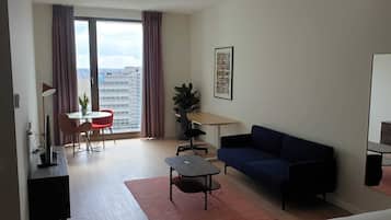 Una sala moderna con un sofá, una mesa de comedor con sillas, una pequeña mesa de centro, un televisor y un ventanal con cortinas.