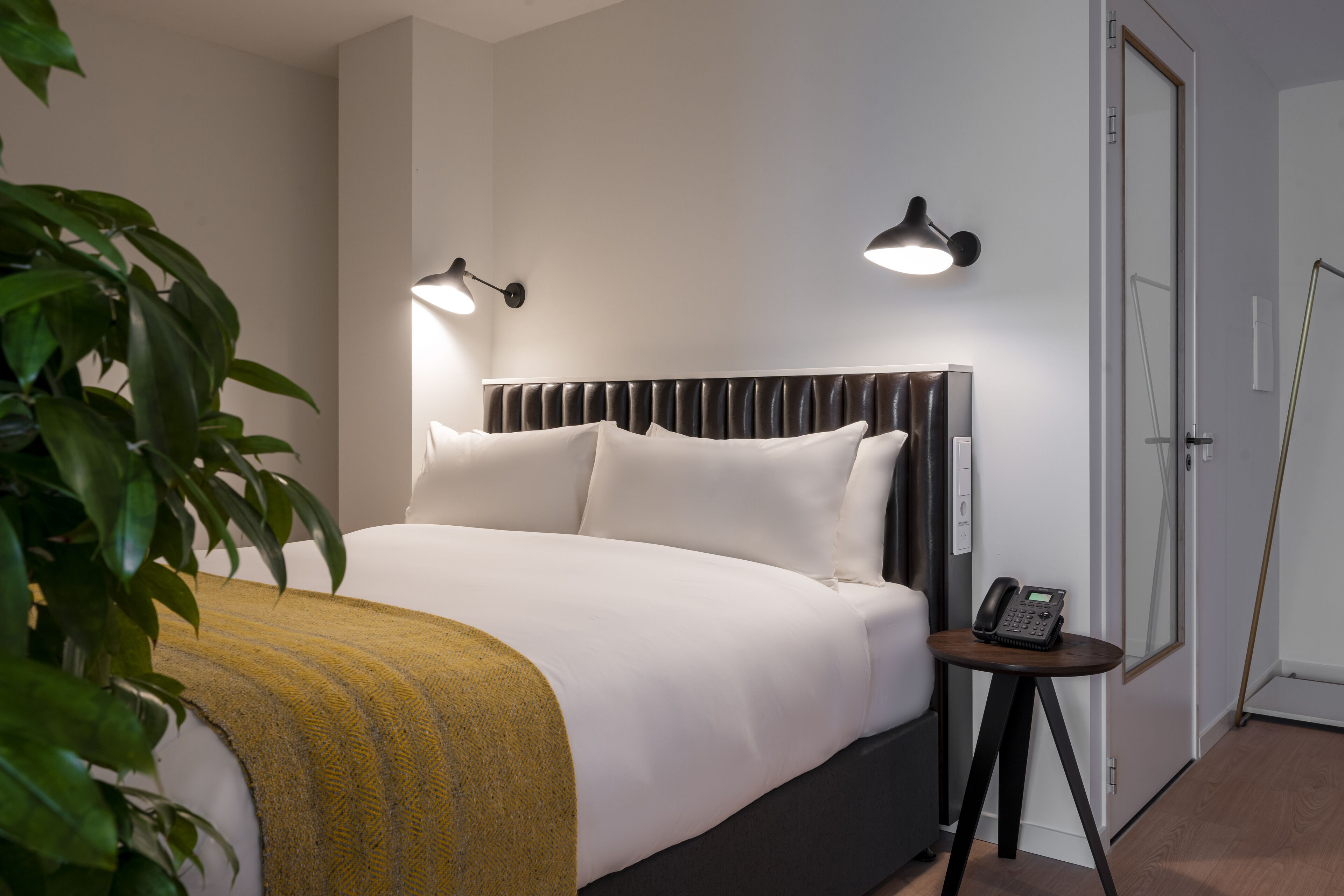A neatly made bed with a headboard, two bedside lamps, a bedside phone, and a small table.