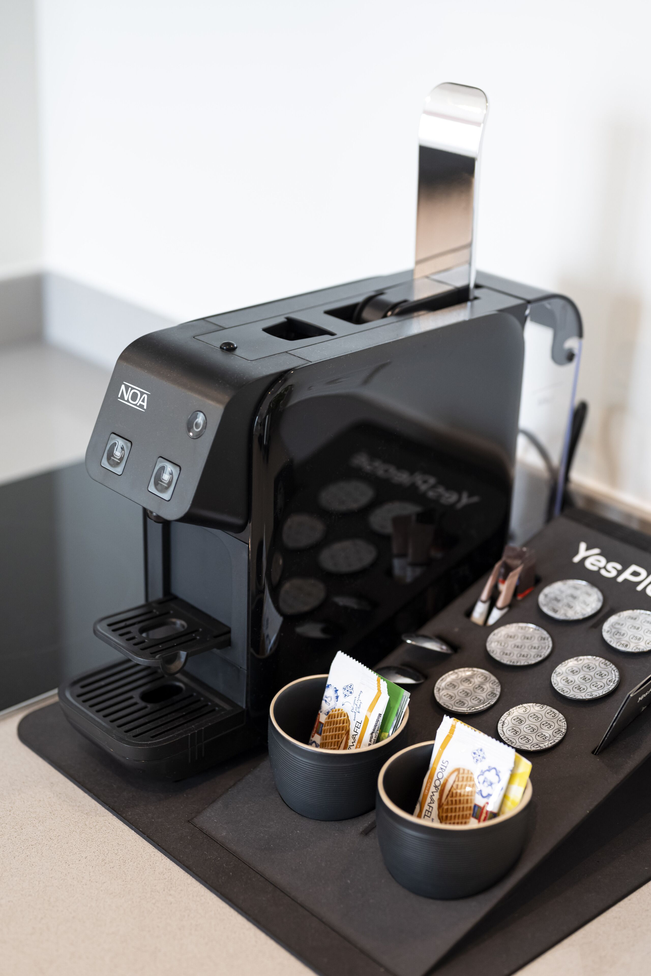 A coffee machine with two cups of coffee and a tray with coffee pods.