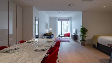 A modern hotel room with a dining area, a bed, a TV, and a plant.