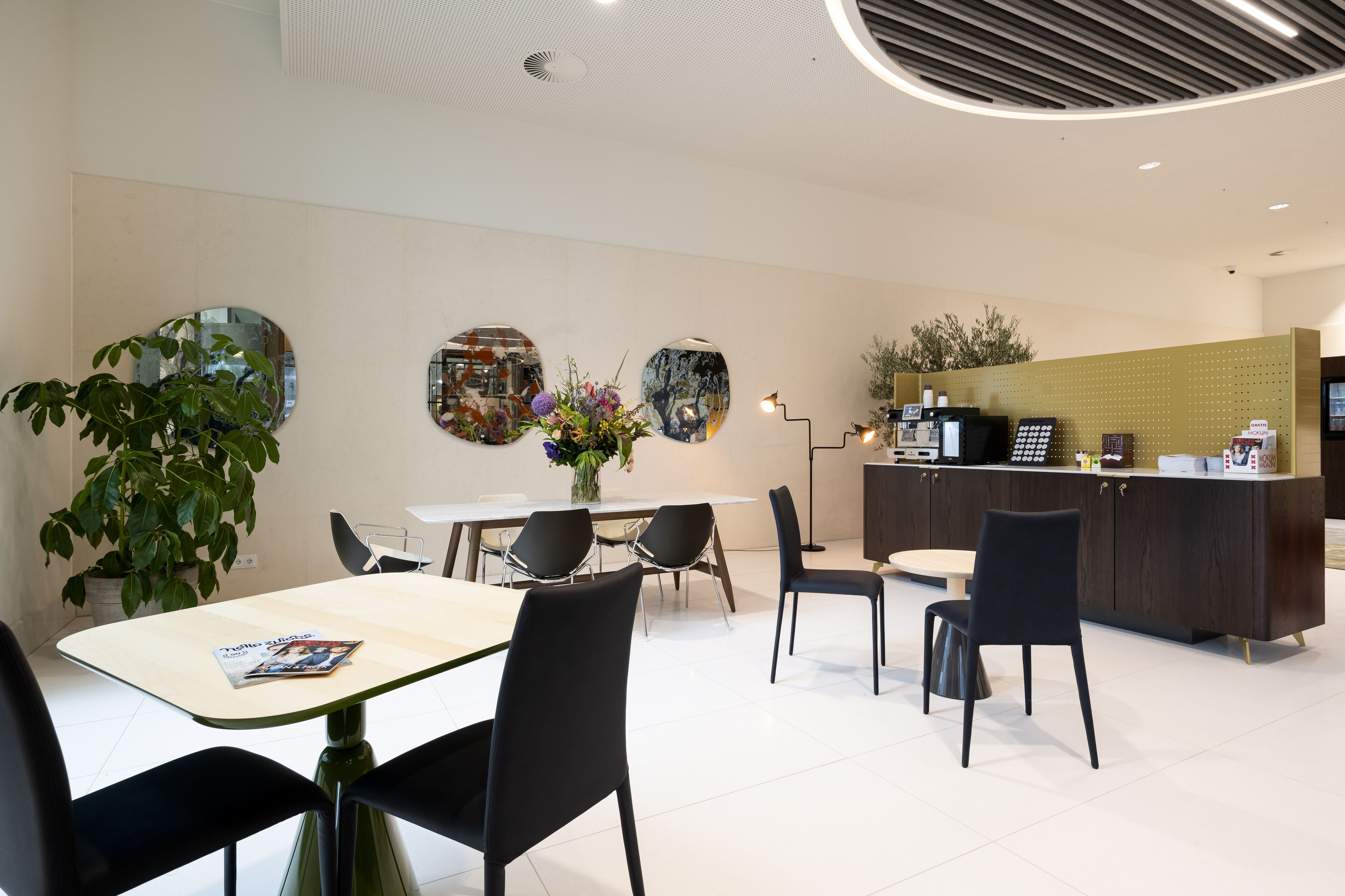 Un moderno vestíbulo de hotel con zona de comedor, mostrador de recepción y una gran planta en maceta.