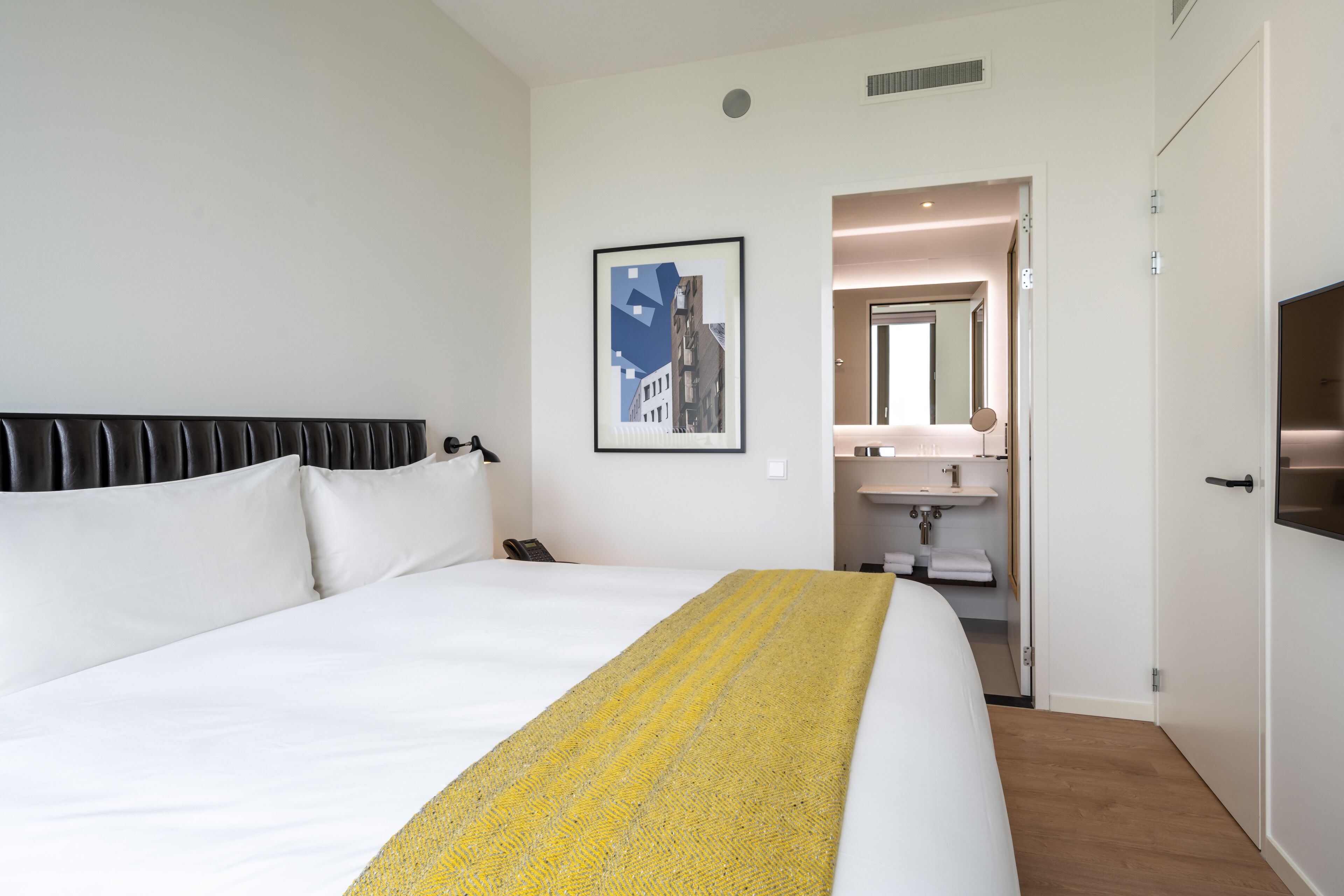 A hotel room with a large bed, a bedside table, a mirror, and a bathroom visible through an open door.