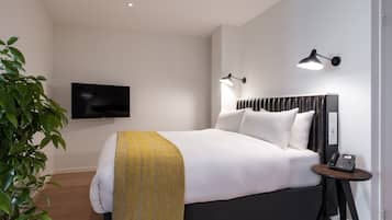 Habitación de hotel moderna con una cama grande, una mesita de noche con un teléfono, un televisor montado en la pared y una planta.
