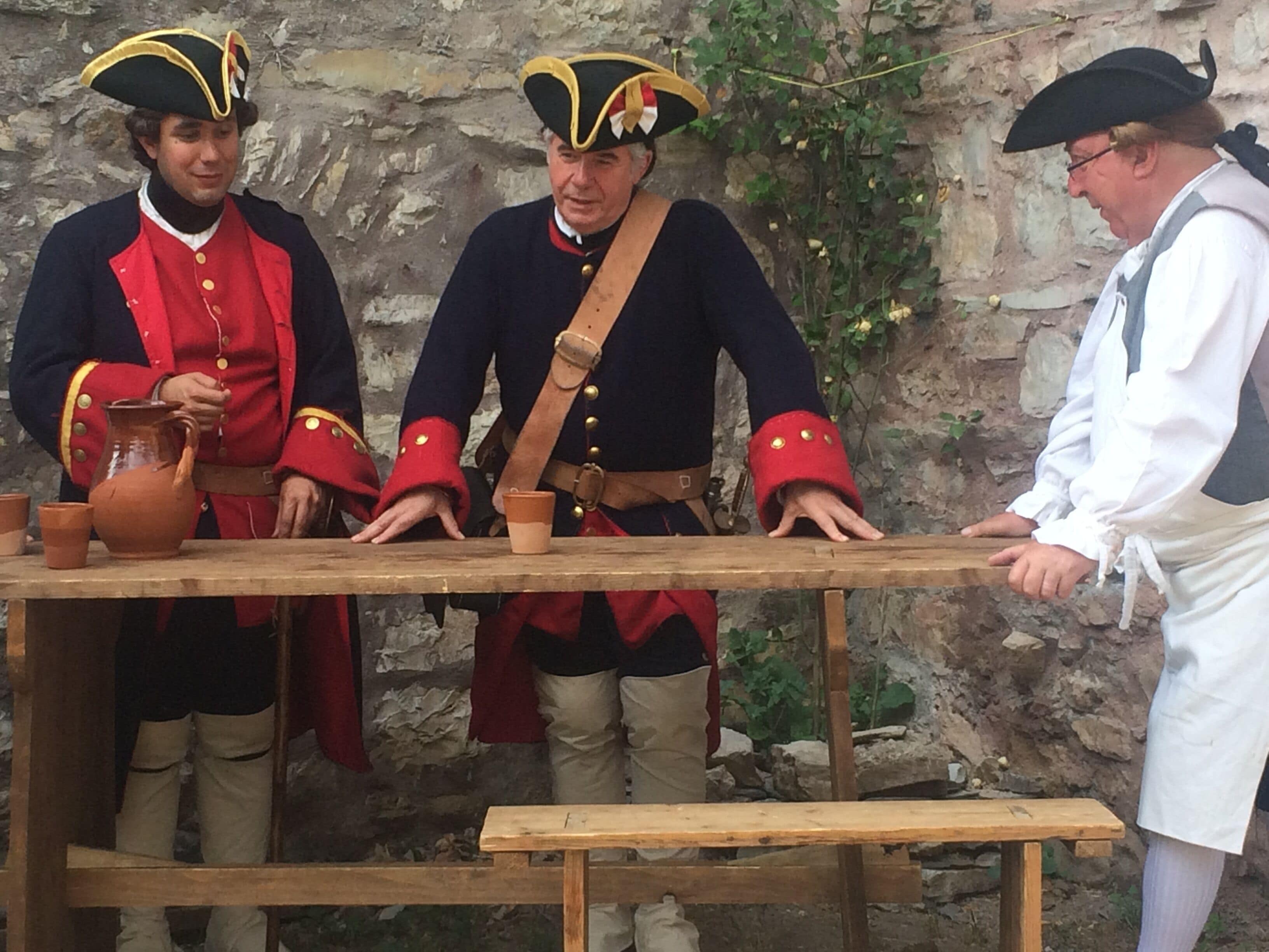 Tres personas con vestimenta histórica frente a una mesa de madera con objetos de cerámica.