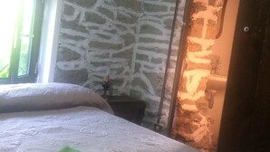 A room with a stone wall, a bed with a patterned bedspread, and a window with a view of greenery. - Baldo e Chicca Bed & Breakfast (Ne)