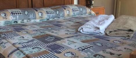 Una cama con una colcha estampada, un cabecero de madera, una mesita de noche con una lámpara y un cuadro enmarcado en la pared.