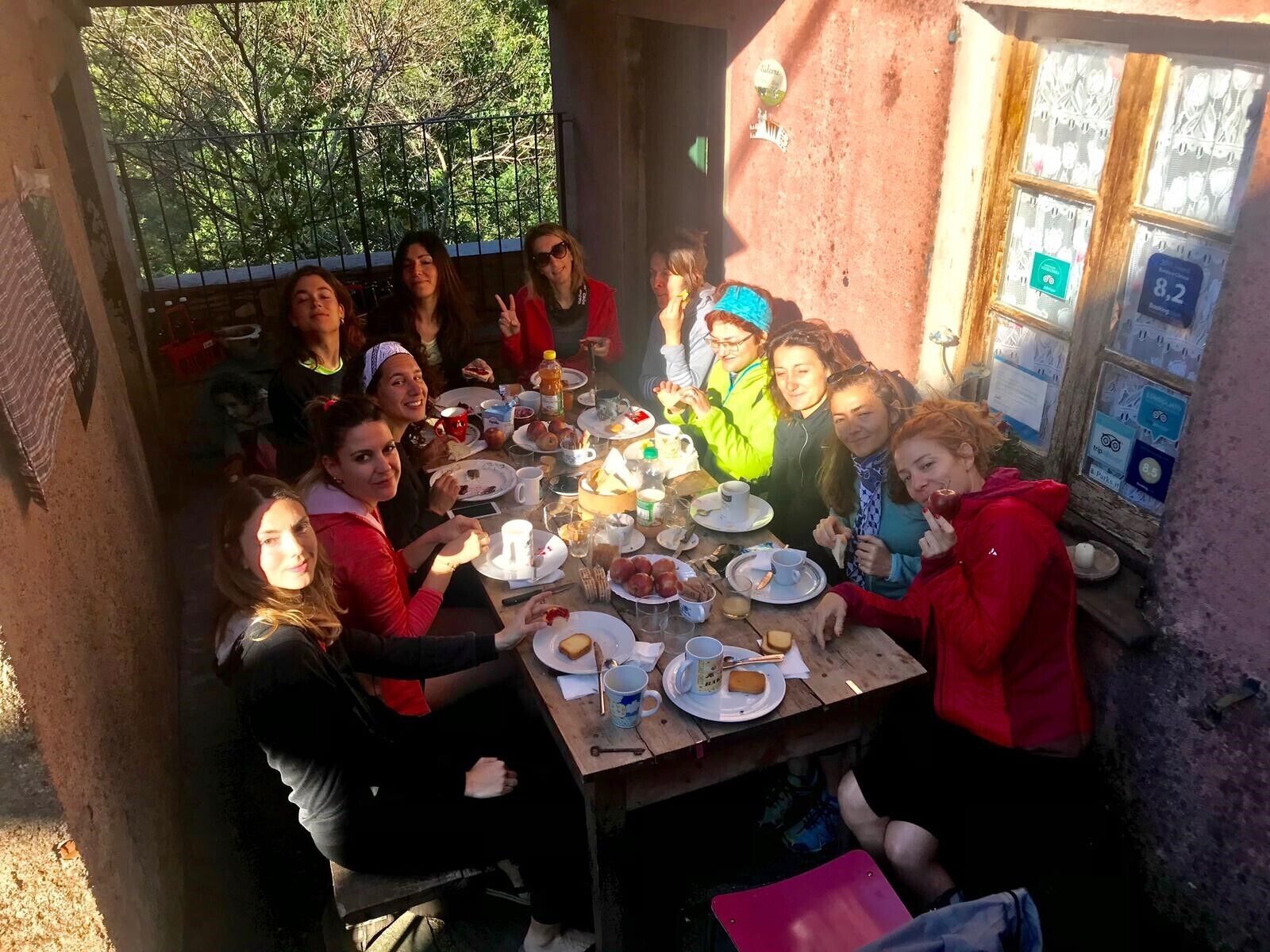 Un grupo de personas sentadas alrededor de una mesa de madera al aire libre, comiendo y bebiendo.