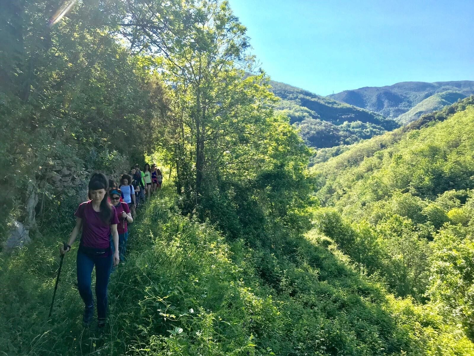 Eine Gruppe von Wanderern auf einem schmalen Pfad, umgeben von üppiger Vegetation und Hügeln.
