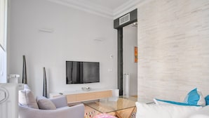 Ein modernes Wohnzimmer mit Flachbildfernseher, einer Couch, einem Sessel und einem Couchtisch.