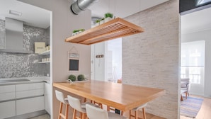 Eine moderne Küche mit einem Holztisch, Barhocker, einer Pendelleuchte und einer Backsteinwand.