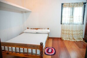 A single bed with a wooden frame, white bedding, and a small rug on a wooden floor. - Mango Tree House (Galle)