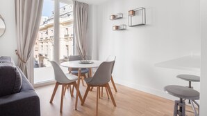 Una sala de estar moderna con una mesa de comedor redonda, sillas grises, un sofá gris y una pequeña zona de bar.
