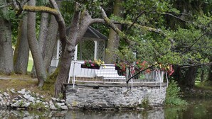 Un ponte di pietra sopra un fiume tranquillo, circondato da vegetazione lussureggiante e un gazebo con fioriere.