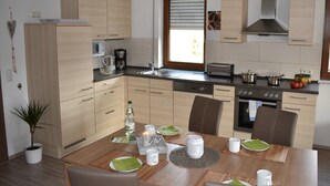 Una cucina moderna con mobili in legno, forno integrato e zona pranzo per quattro persone, con tavolo, sedie e macchina da caffè.