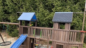 Una struttura giochi in legno con uno scivolo blu e due casette.