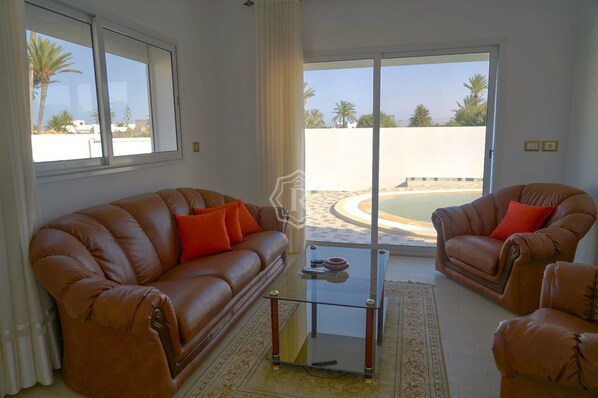 A living room with a brown leather sofa, two armchairs, and a glass coffee table.