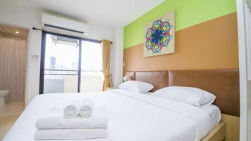 A hotel room with a bed, a large window, a painting on the wall, and a view of the city.